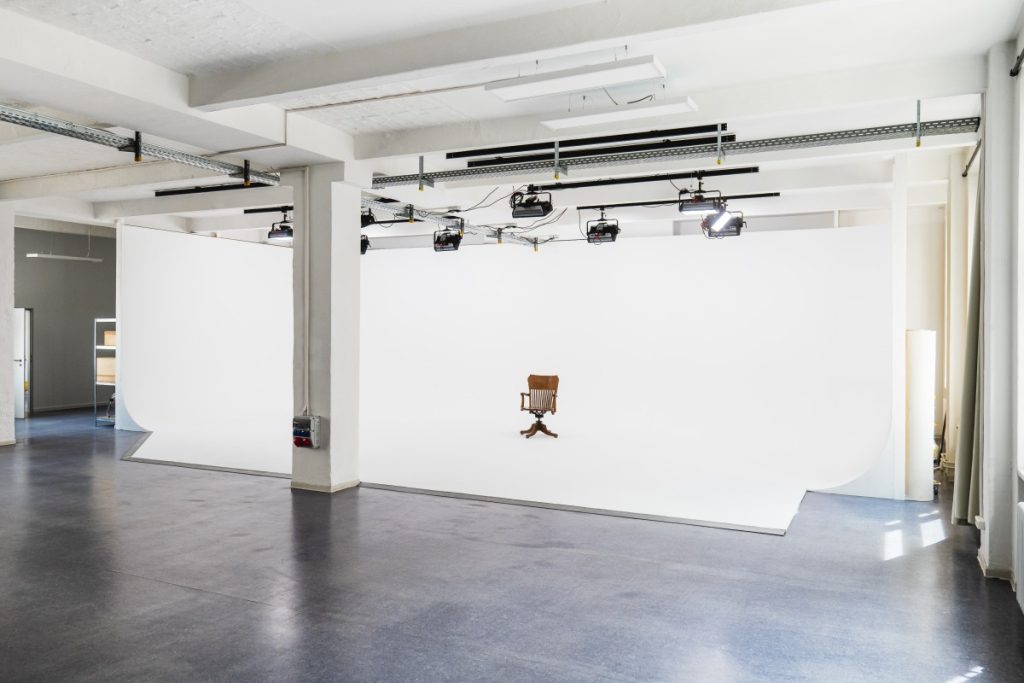 We see the whole white cyclorama of the Neon Island studio and Apurture lights hang from the ceiling.