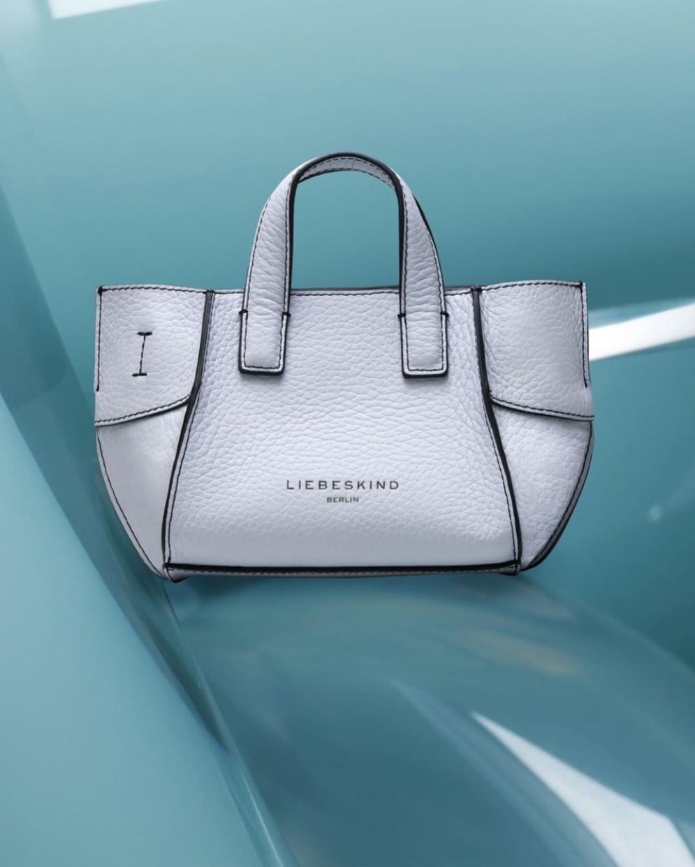 white leather handbag by Liebeskind on turquoise plexiglass background