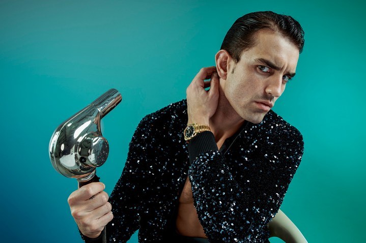a man wearing a Rolex styles his hair with a retro hair dryer